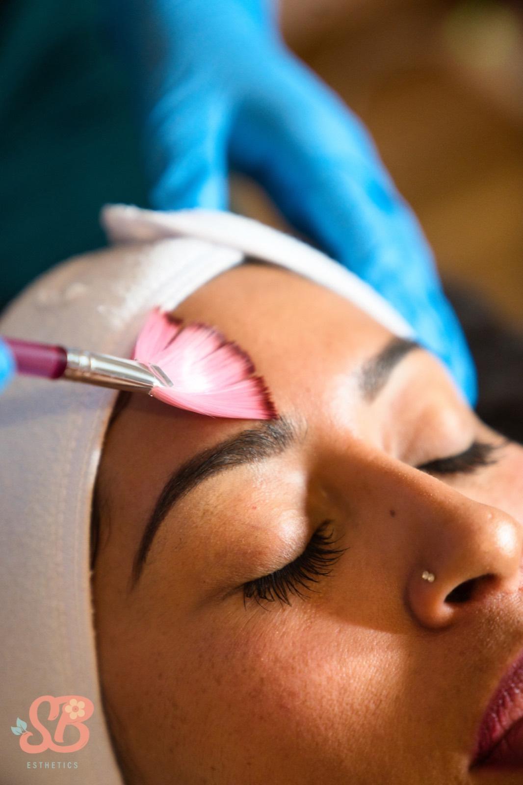 A fan brush applying a treatment mask across a client's brow during a custom facial.